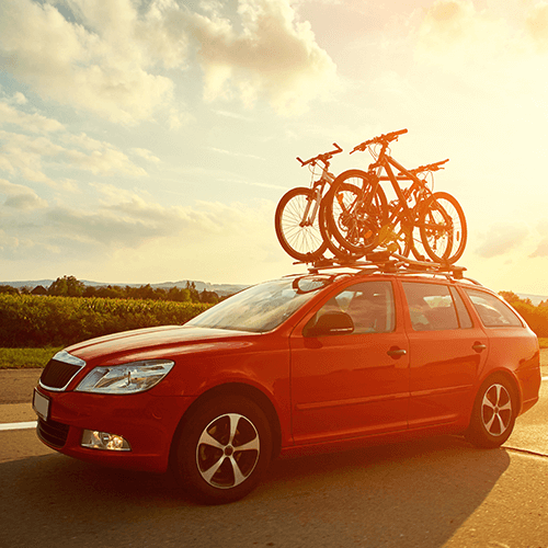 Red family sedan with a bike rack on top driving on a road