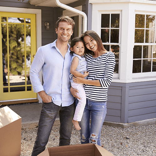 Mom and dad holding their child while standing in front of a house