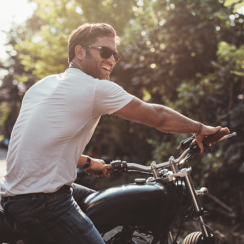 Smiling man with a white shirt and sunglasses riding a black motorcycle